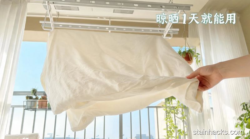 阳台晾衣架区域场景，平铺在晾衣架上的纯棉床单，人手轻轻调整拉伸床单边角的动作，配有文字「晾晒1天就能用」，风格清新明亮生活化，关键元素：方便、省时间
